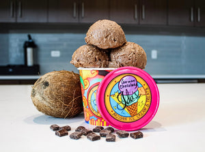 German chocolate ice cream scoops in an Ida's Artisan Ice Cream cup alongside a fresh, whole coconut surrounded by chocolate chunks